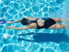 A woman in a swimsuit doing swimming exercises in clear blue water to support back pain relief and relaxation.