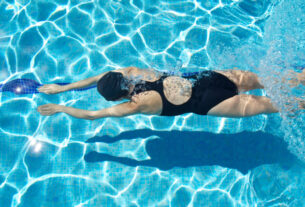 A woman in a swimsuit doing swimming exercises in clear blue water to support back pain relief and relaxation.